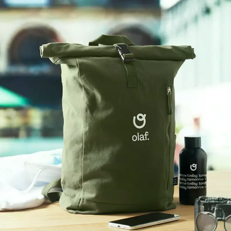 Mochila verde "olaf." enrollable con botella, móvil y otros objetos sobre una mesa.