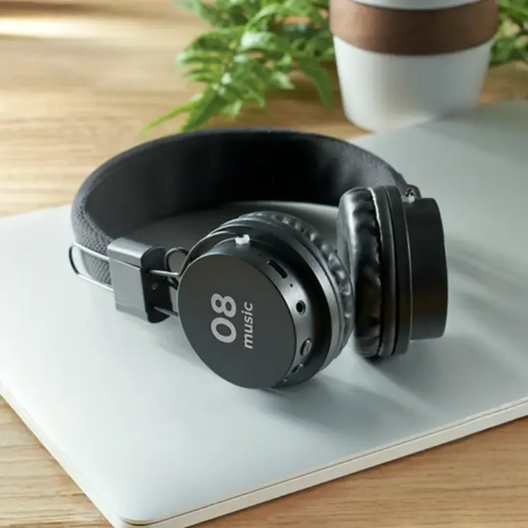 Auriculares negros "08 music" sobre una laptop blanca en un escritorio de madera.