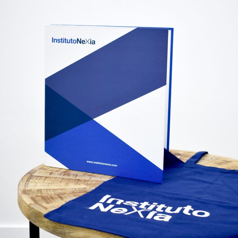 Un libro y una bolsa azul con el logo "Instituto Nexia" sobre una mesa redonda de madera.