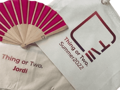 Un abanico rosa y bolsas de tela con texto "Thing or Two" y "Summer 2022".