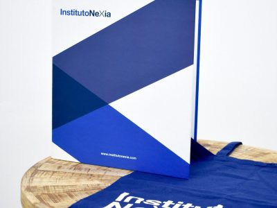 Un libro y una bolsa azul con el logo "Instituto Nexia" sobre una mesa redonda de madera.